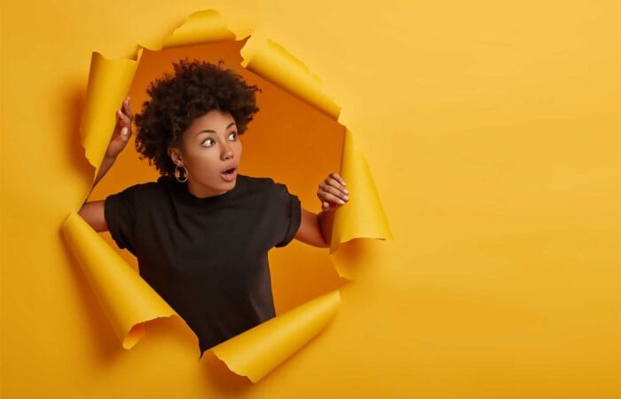National Arts Fundraising School - Woman poking head through paper tear hole on orange background.
